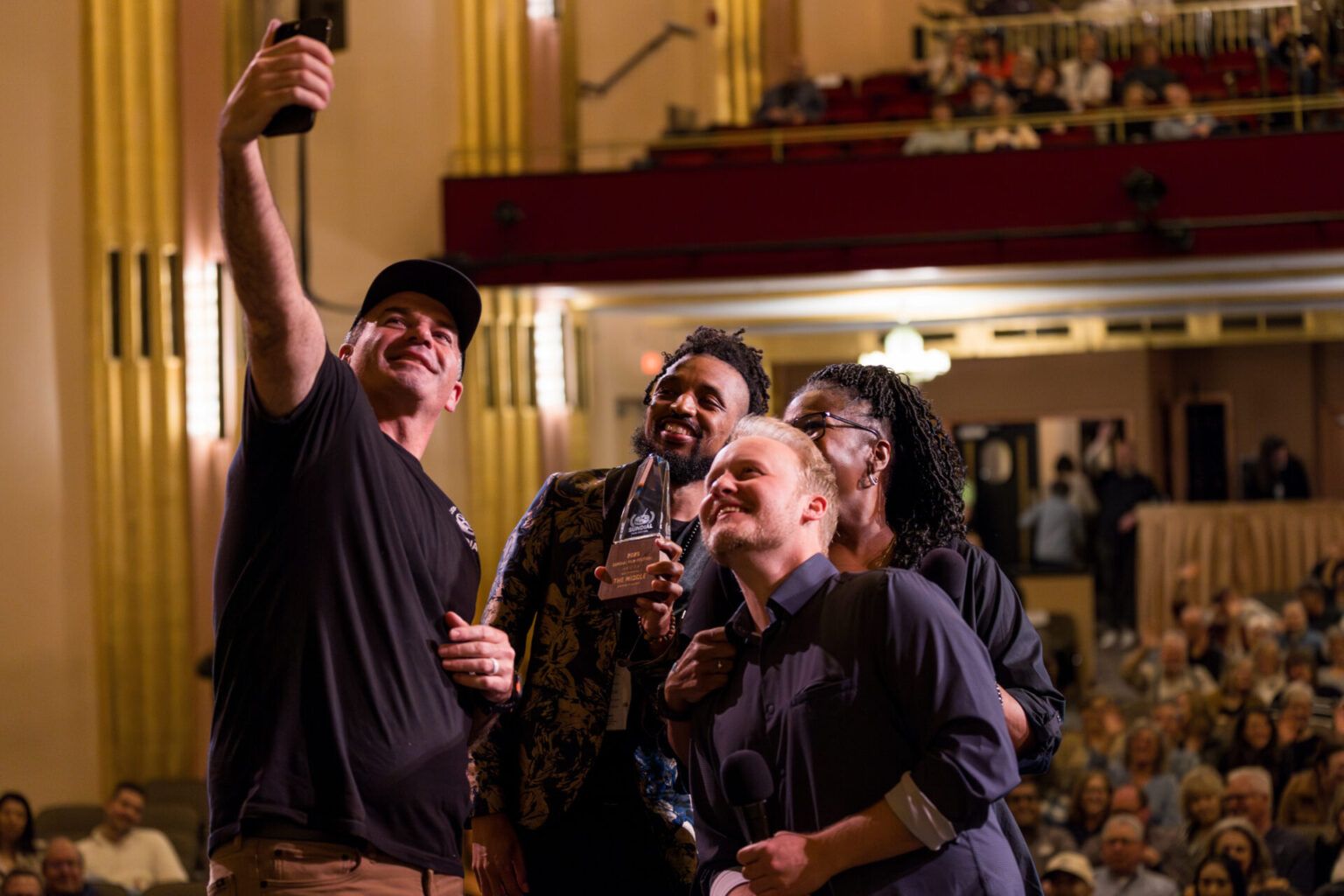 Filmmakers take a selfie on the Cascade stage with an award in front of the audience